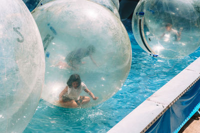 Woman sitting in zorb ball floating on swimming pool