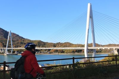 Cyclist by cable stayed bridge over river against clear sky