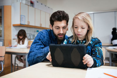 Male teacher explaining student in using digital tablet at classroom