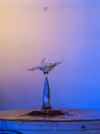 Close-up of drop falling on water against blue background