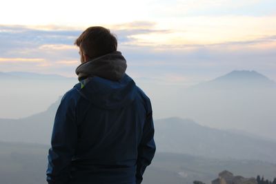 Rear view of man standing on mountain against sky