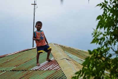 Low angle portrait of boy standing against sky