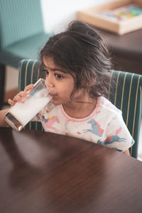 Girl drinking milk while sitting on table at home