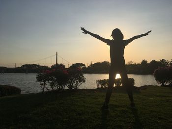 Silhouette person standing on riverbank against sky during sunset