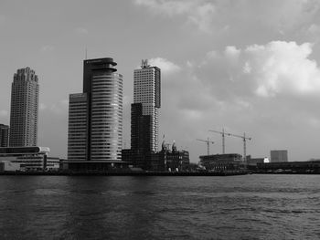 Modern buildings by river against sky in city