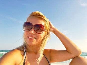 Smiling beautiful woman sitting against sea at beach