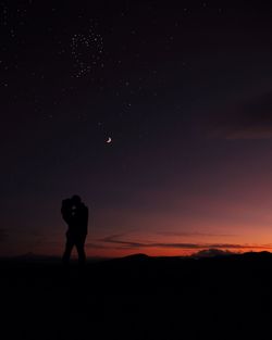 Silhouette couple standing against star field during sunset