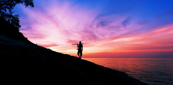 Silhouette man standing at beach against sky during sunset