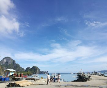 People on walkway by sea against blue sky