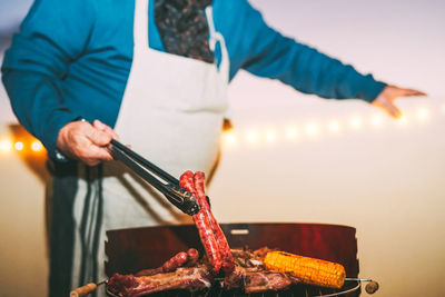 Midsection of man preparing sausage on barbecue grill