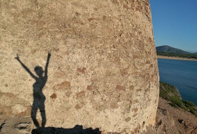 Shadow of man on cliff by sea against sky