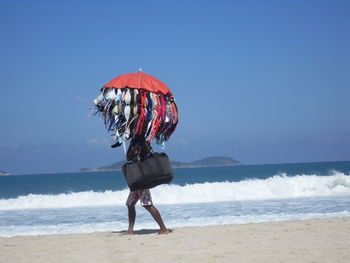 Vendor selling bras hanging on umbrella at beach against clear sky