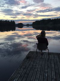 Rear view of woman sitting on jetty against lake