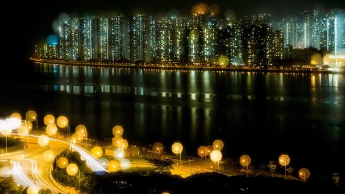 Illuminated city by river against sky at night