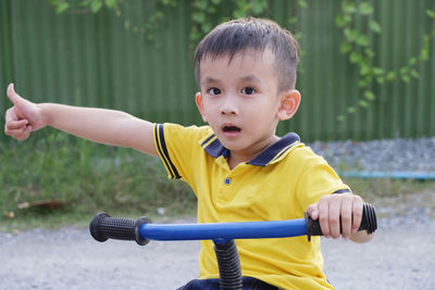 Portrait of cute boy showing thumbs up while riding bicycle on road