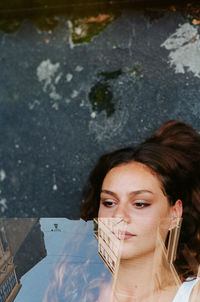 High angle view of young woman lying on road with reflection on glass