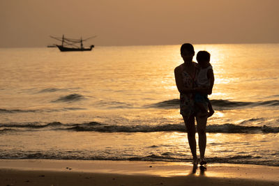 Rear view of man standing on beach against sky during sunset