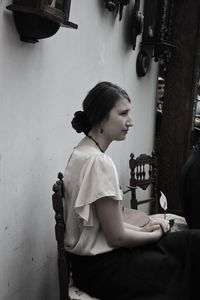 Side view of thoughtful young woman sitting on chair at home