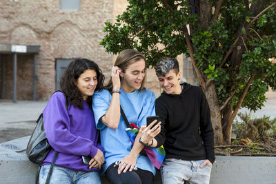 Friends using mobile phone while standing outdoors on the street.