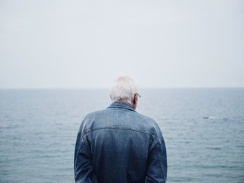 Rear view of man standing in sea against clear sky