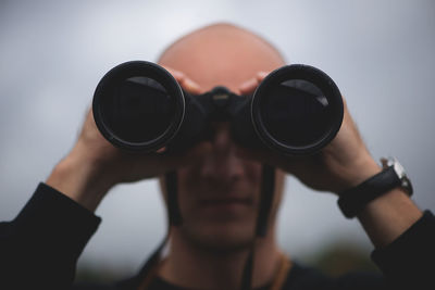 Close-up of mid adult man looking through binoculars while standing against sky