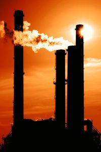 Low angle view of silhouette smoke stack emitting smoke against sky during sunset