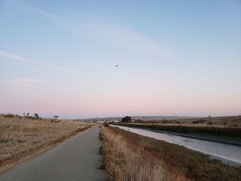 Road by field against sky during sunset