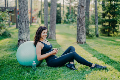 Woman with smart phone sitting by fitness ball in park