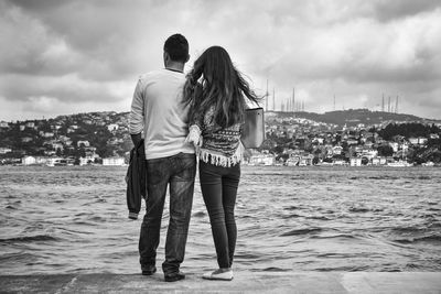 Rear view of couple walking on beach against sky