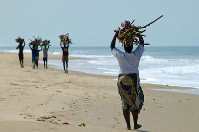 Rear view of friends standing on beach against sky