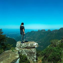 Rear view of man standing on rock against blue sky