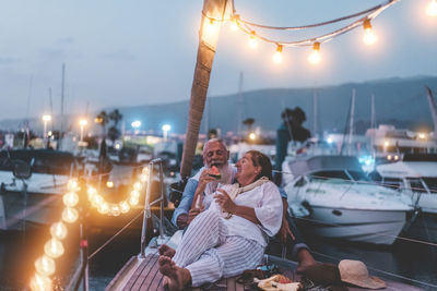 Senior man with woman relaxing in boat at harbor during dusk