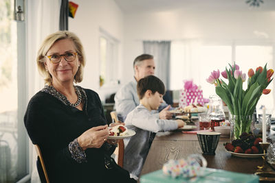 Portrait of smiling grandmother having cake while sitting with family at table during party