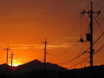 Silhouette electricity pylons and mountains against orange sky