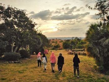 Rear view of people walking on field against sky