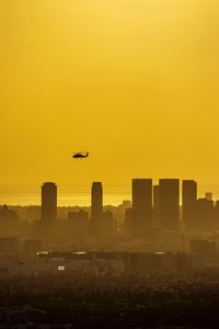 Airplane flying over city against clear sky during sunset