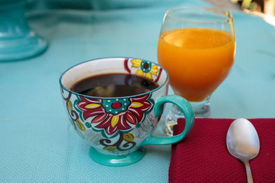 Black coffee in a colorful flower print cup with orange juice on a blue table cloth