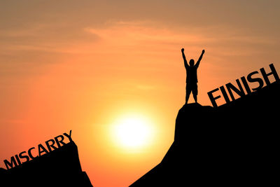 Silhouette man standing on rock against orange sky