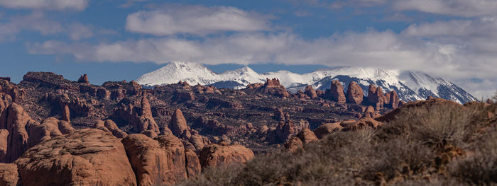 Panoramic scene of rugged red sandstone terrain with white snow capped mountains in the background