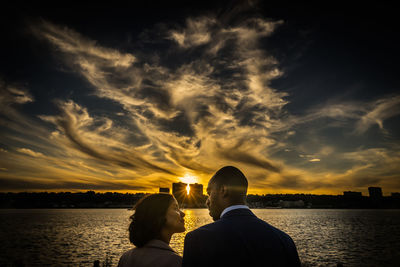 Rear view of couple by sea against sky during sunset