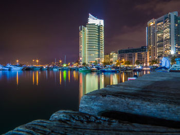 Illuminated buildings by sea against sky at night