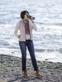 Smiling woman walking on seaside with metal travel mug. vacation on ocean coast. turquoise water.