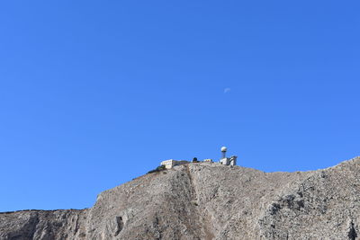 Low angle view of man on rock against clear blue sky