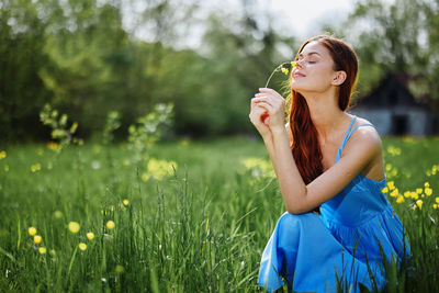 Young woman drinking water while sitting on field