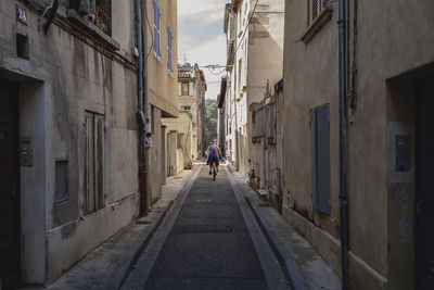 Rear view of woman riding bicycle amidst buildings at alley in city