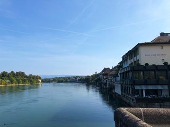 Scenic view of river by buildings against blue sky