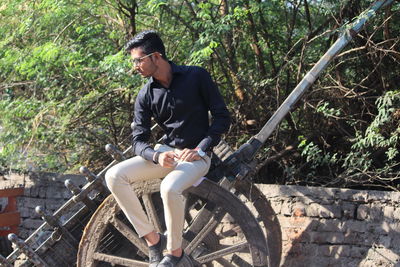 Full length of young man sitting on old push cart