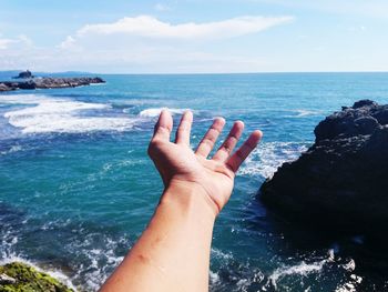 Close-up of hand against sea and sky