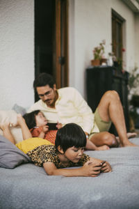 Girl using smart phone while down syndrome girl talking to father on sofa at home