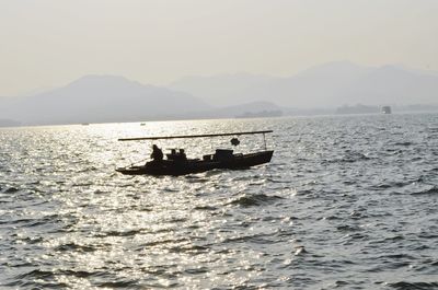 Silhouette people in boat on sea against sky